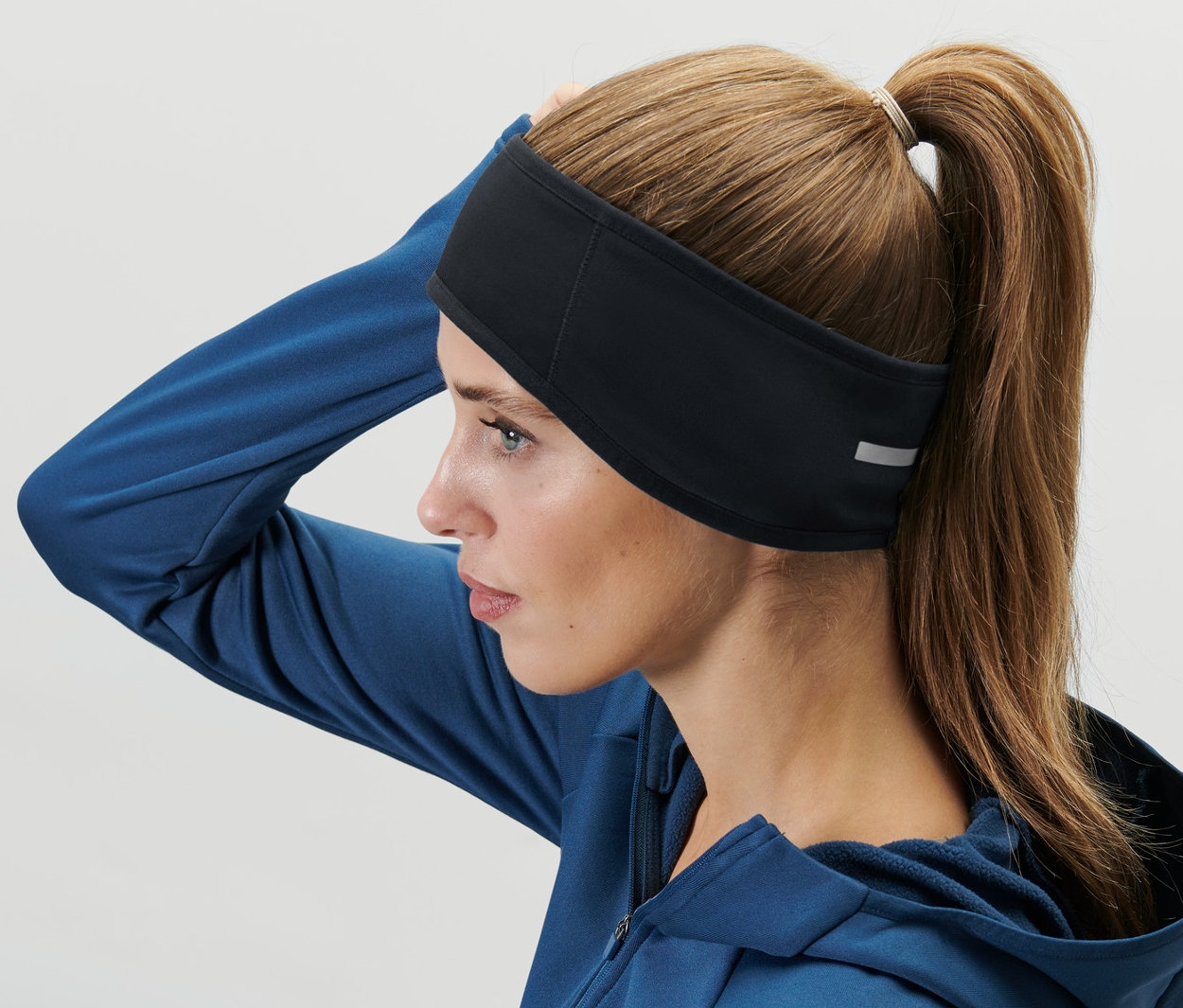 Frau mit braunen Haaren, die zu einem Pferdeschwanz zusammengebunden sind, trägt ein Windprotection-Stirnband.