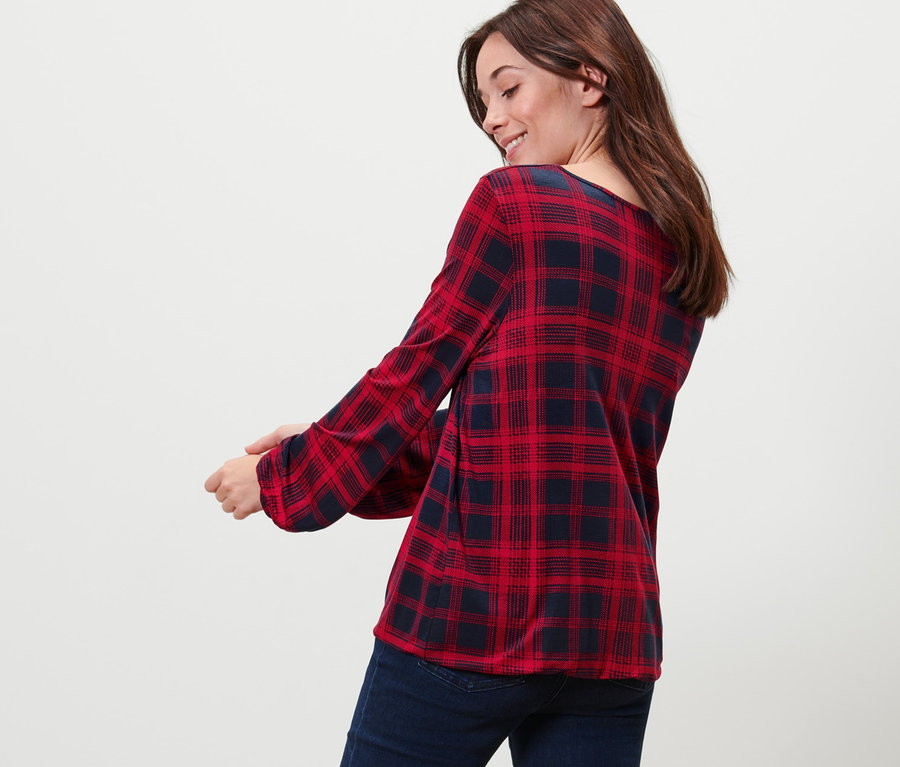 Frau blickt über die Schulter und trägt ein kariertes Blusenshirt und Jeans.