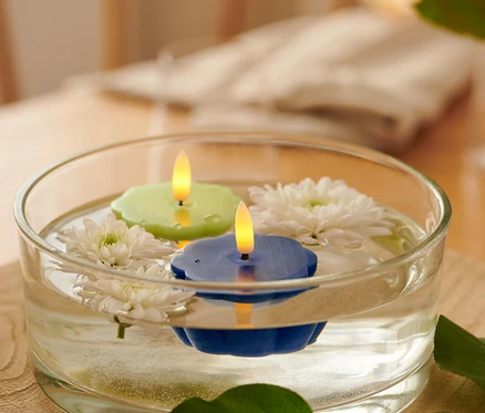 In einer Glasschale schwimmen zwei LED-Echtwachs-Teelichter, ein grünes und ein blaues, und weiße Blumen.