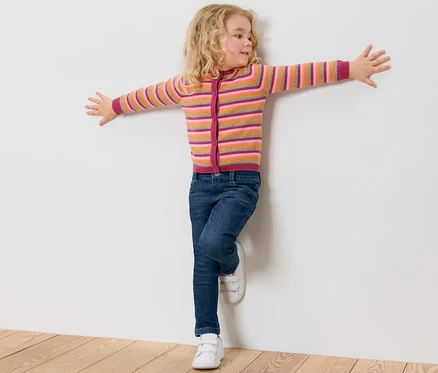 Mädchen lehnt in Kinder-Jeans ‒ Fit »Lotta« an einer weißen Wand.