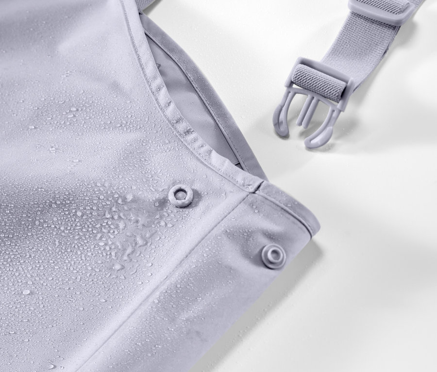 Detailaufnahme einer Kinder-Regenhose mit Trägern, auf der sich Wassertropfen befinden.