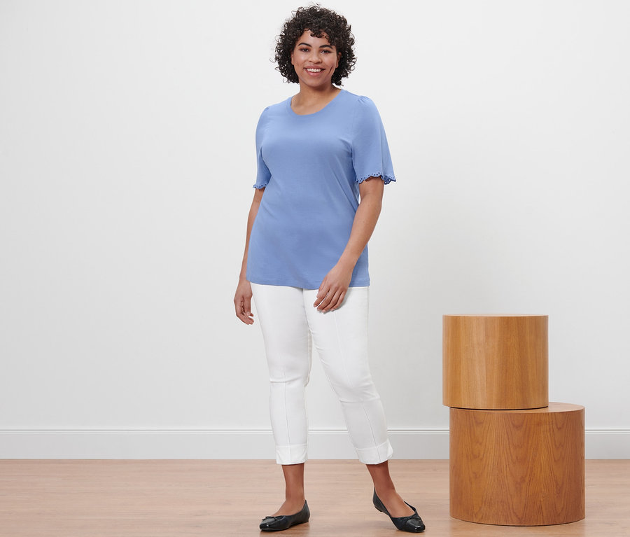 Frau posiert in hellblauem Shirt mit Raffung und weißer Stretchhose.