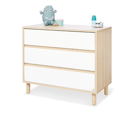 Eine Kommode mit drei Schubladen in Holz- und Weißtönen. Auf der Kommode liegen ein Stofftier, eine Dose und eine Babyflasche.