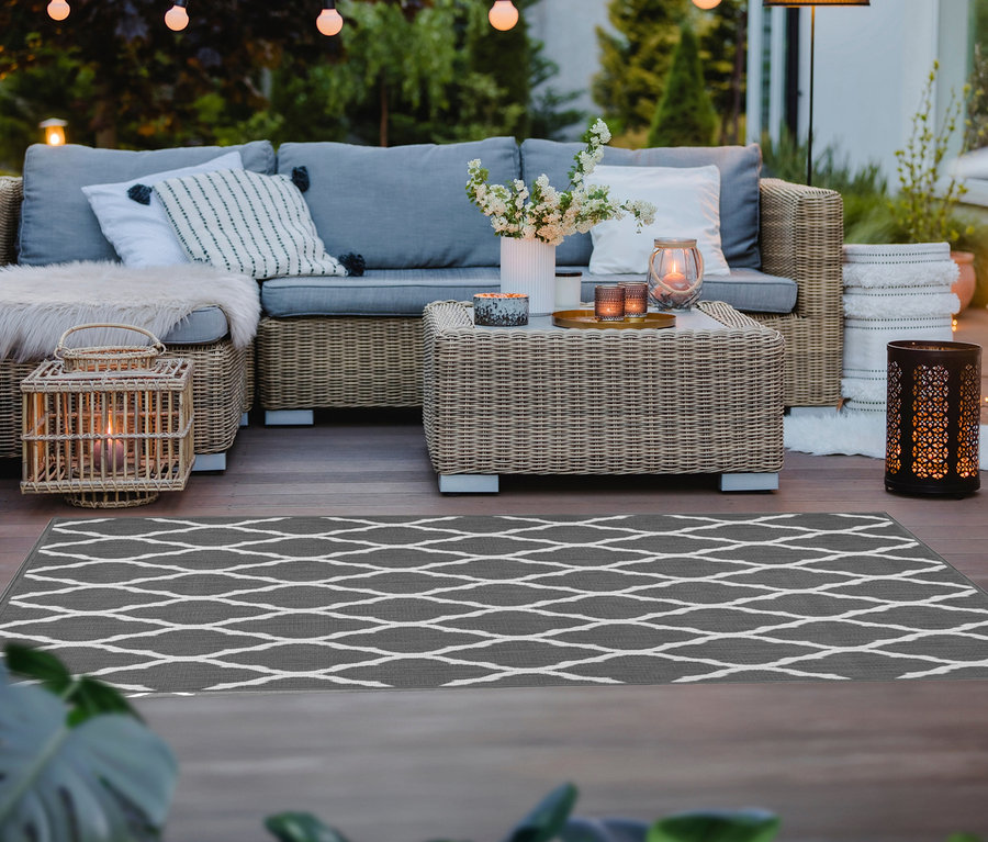 Grauer Outdoor-Wende Teppich »Rhombus« (ca. 120 x 160 cm und ca. 160 x 220 cm) auf einer Terrasse mit Rattanmöbeln und Lichtern.