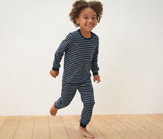 Ein Junge in einem blau gestreiften Pyjama rennt auf einem Holzboden. 2 Kinder-Pyjamas, blau.