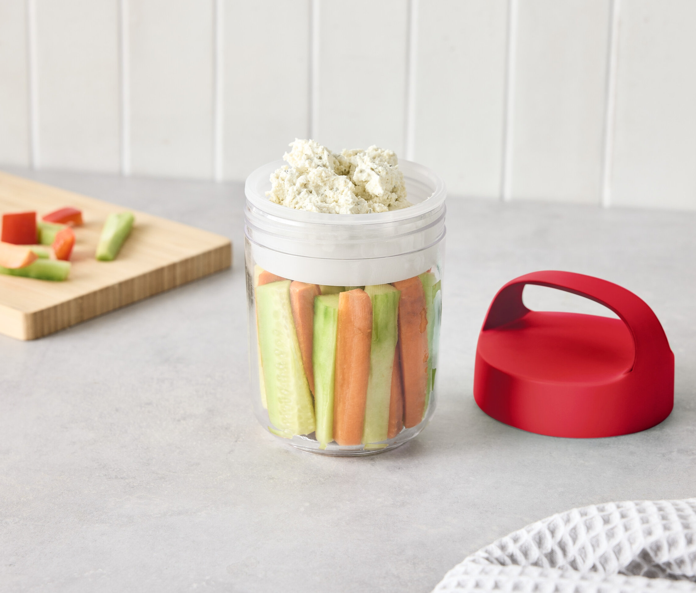 Ein Glas mit geschnittenem Gemüse und Dip auf einem Tisch.