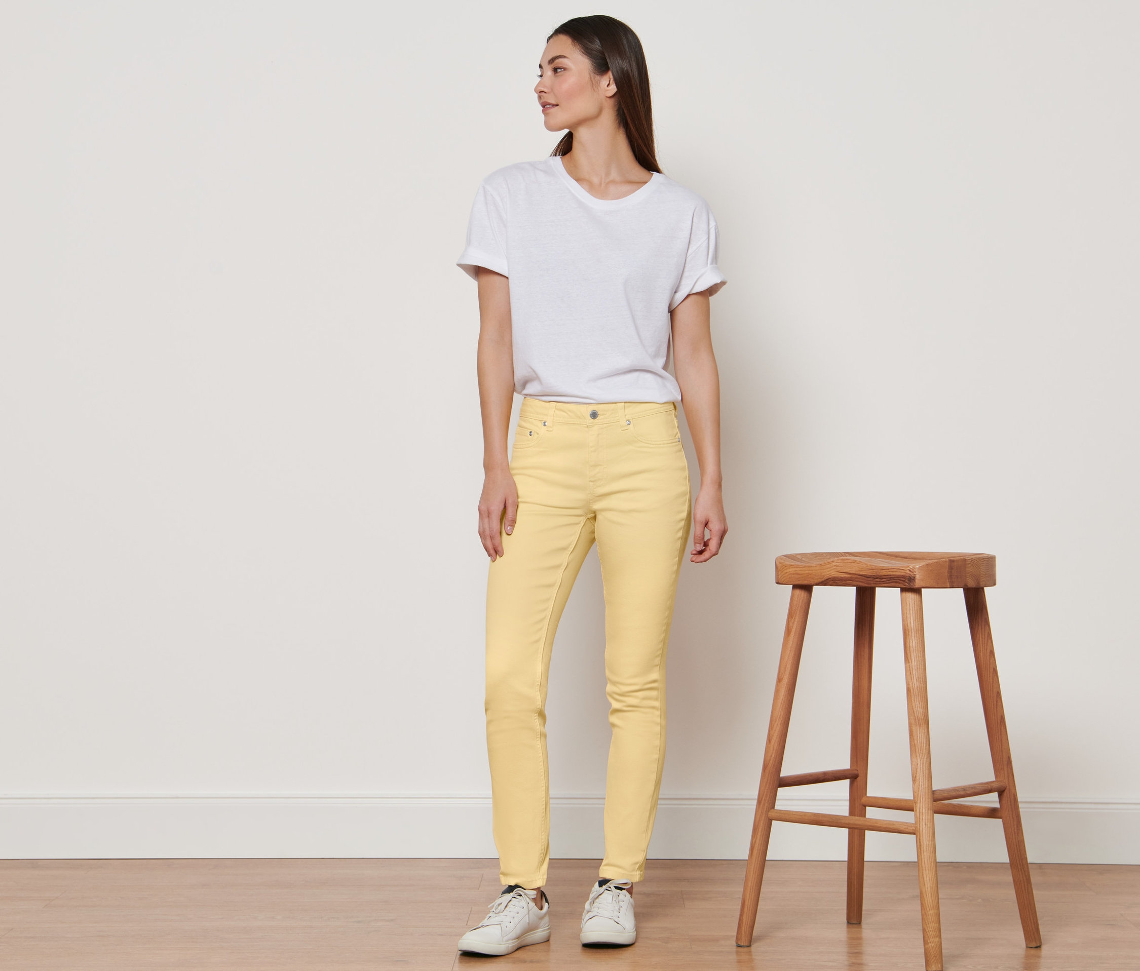 Frau steht und trägt gelbe Denim »Fit Emma« und ein weißes T-Shirt.