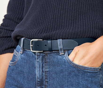 Frau mit Hand in Jeanshosentasche trägt Ledergürtel.