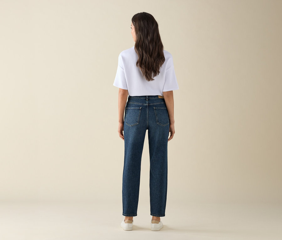 Eine Frau von hinten trägt Mom Jeans – Fit »Nyla«, dark blue, ein weißes T-Shirt und Turnschuhe.