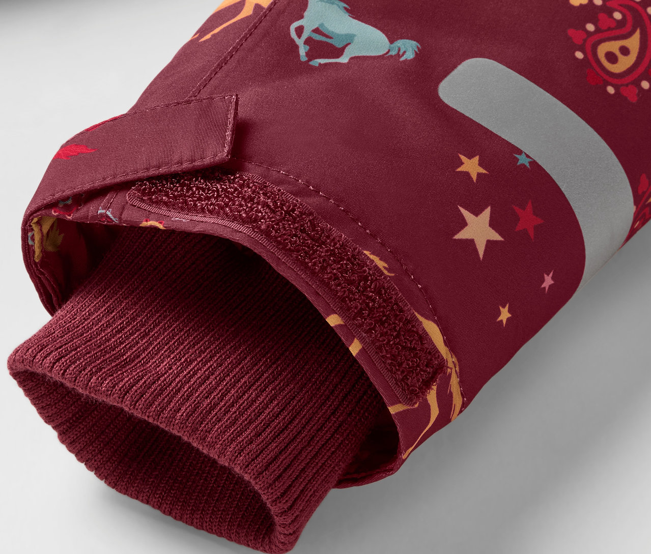 Detail eines bordeauxroten Jackenärmels mit Pferde- und Sternenmuster, abgeschlossen mit einem bordeauxroten Bündchen.