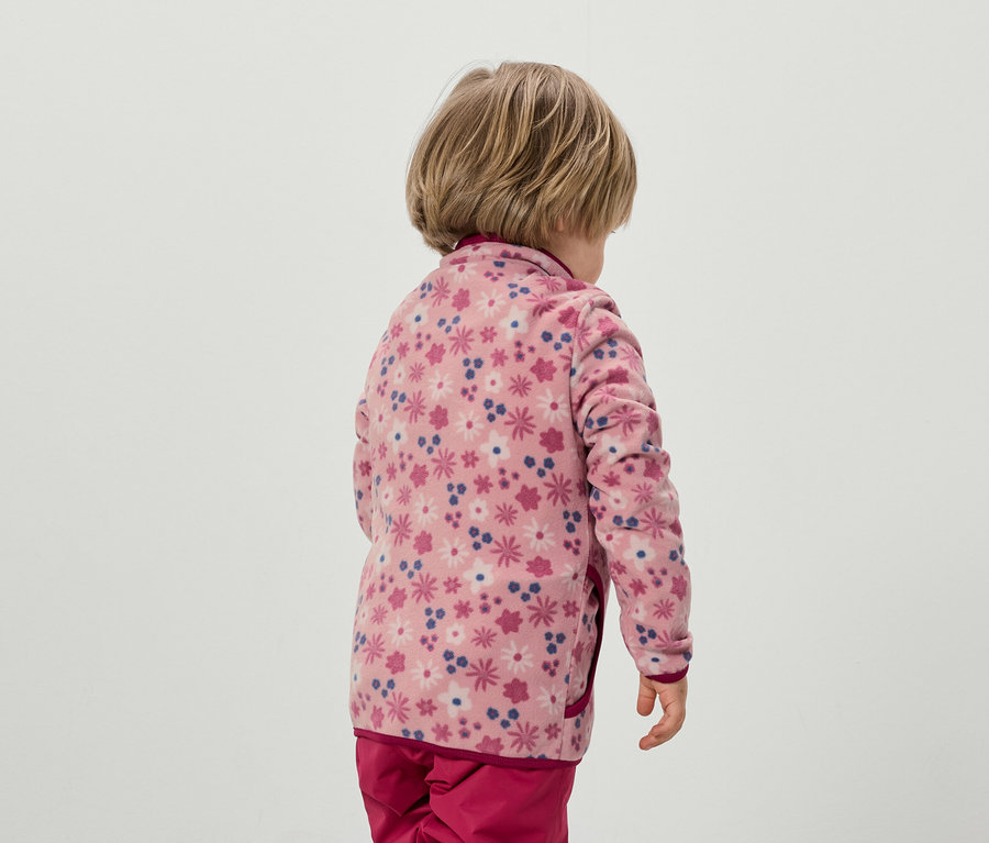 Kind von hinten, trägt eine rosa Fleecejacke mit Blumenmuster und eine rosa Hose.