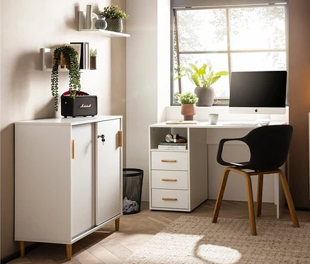 Ein weißer Schreibtisch mit Computer steht an einem Fenster. Neben dem Schreibtisch steht ein weißer Aktenschrank »Torge«.