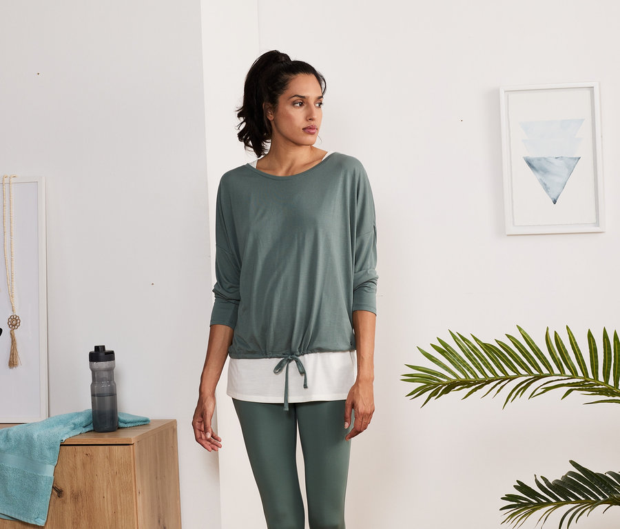 Frau trägt ein grün-weißes 2-in-1-Sportshirt und grüne Leggings.