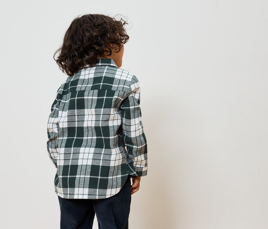 Junge mit dem Rücken zur Kamera trägt ein grün-weiß kariertes Hemd und dunkelblaue Hosen.