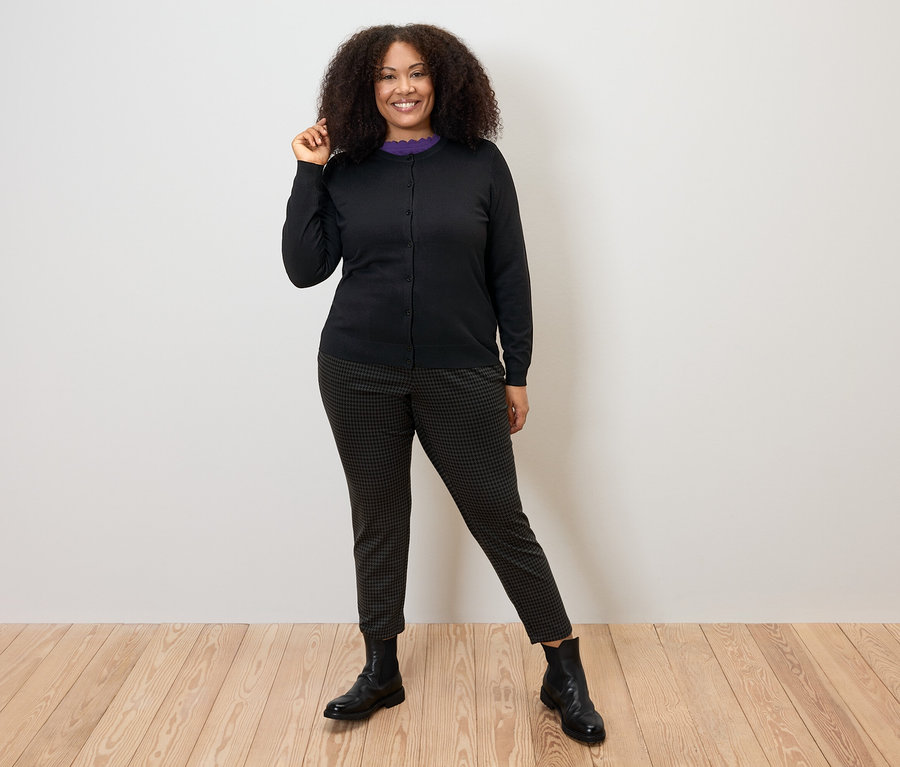 Frau posiert in schwarzem Feinstrick-Cardigan, Hose und Stiefeln.