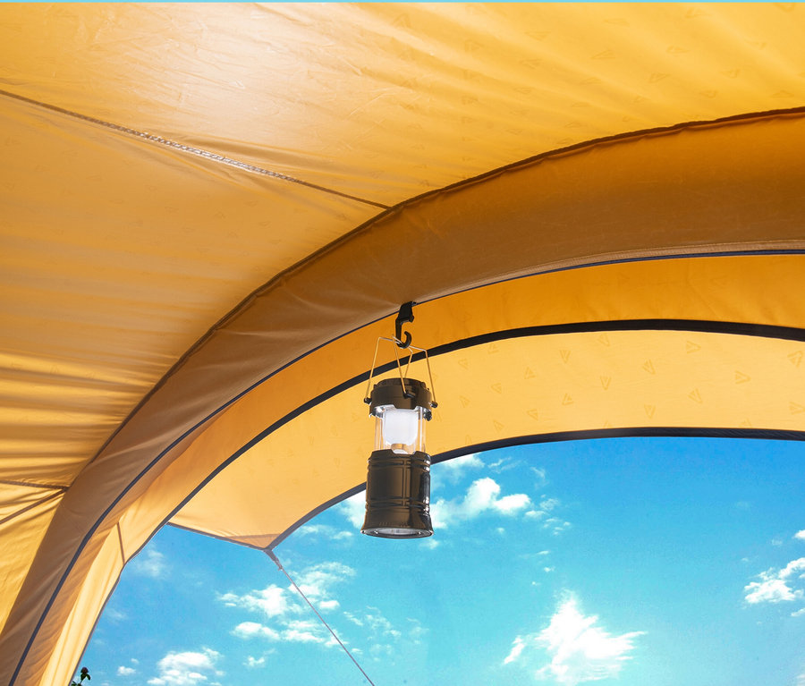 Blick von Innen auf ein gelbes Tambu Bus-Sonnensegel GATI und eine Laterne, die von unten hängt, im Hintergrund blauer Himmel.