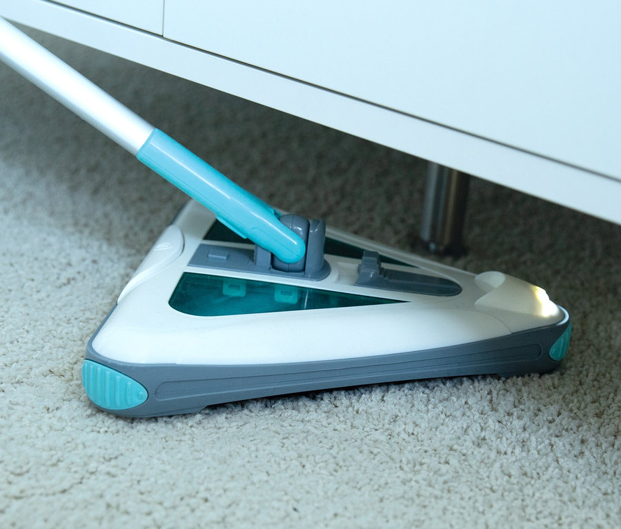 Ein Akkubesen auf einem Teppich unter einem Möbelstück.