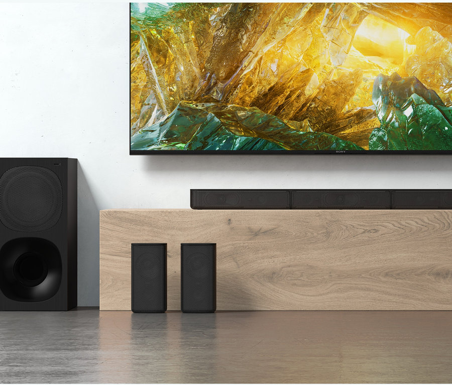 Schwarze Soundbar und Lautsprecher unter einem Fernseher. Eine Sony 5.1.-Kanal-Soundbar »HT-S20R« steht auf einem Holzmöbel.