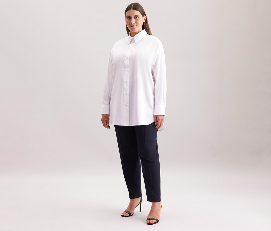 Frau trägt eine weiße Seidensticker Oversize Longbluse, dunkle Hose und schwarze Sandaletten.