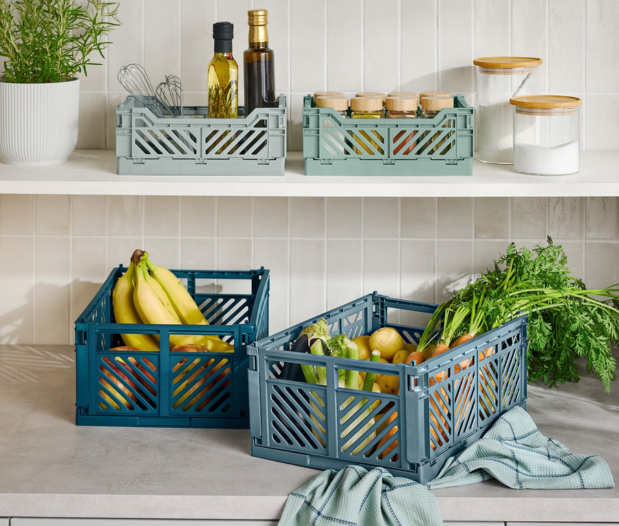 Auf einer Küchentheke stehen drei faltbare Aufbewahrungsboxen, eine blaue mit Bananen, eine graue mit Gemüse und eine graue mit Küchenutensilien.