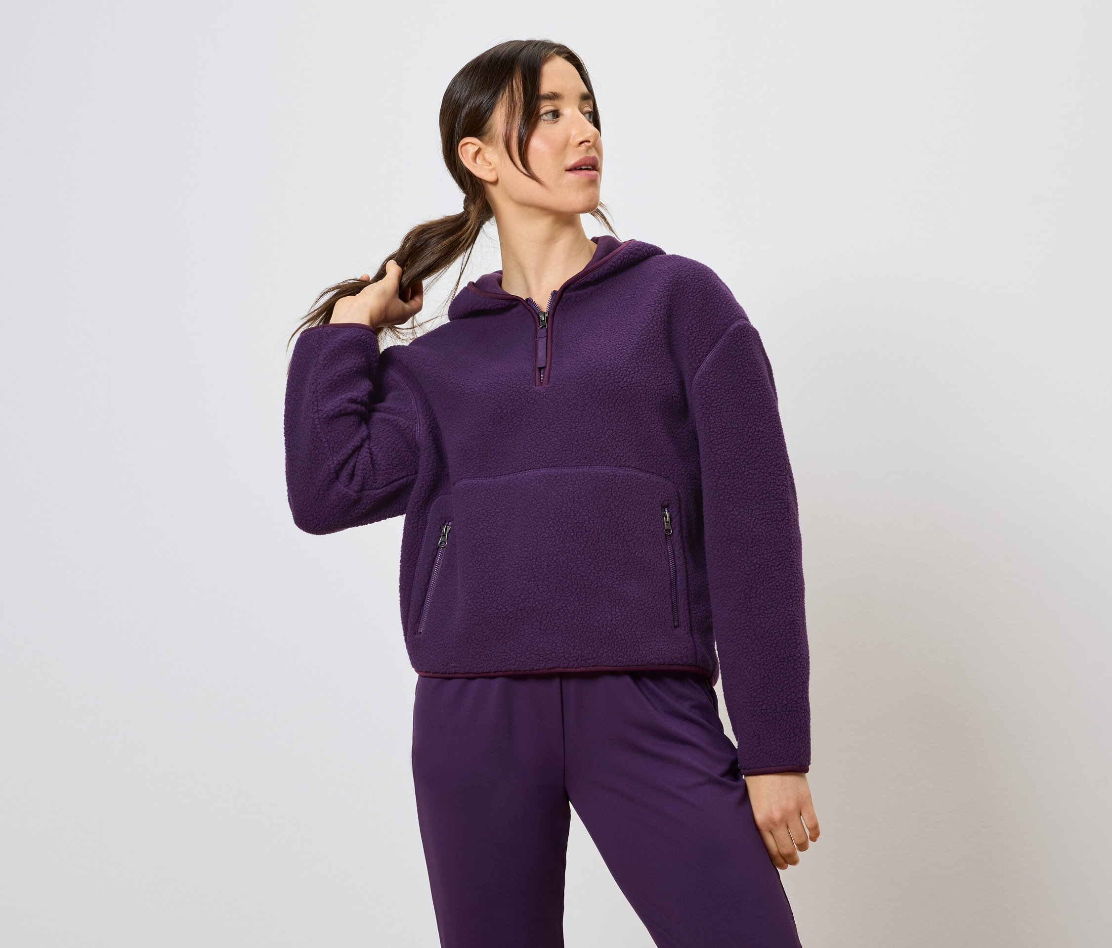 Frau hält Zopf und trägt einen lila Kapuzenpullover und Hose.