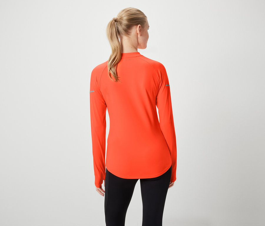 Rückansicht einer Frau mit blonden, zum Pferdeschwanz gebundenen Haaren, die ein orangefarbenes Sportoberteil mit langen Ärmeln und schwarze Leggings trägt.