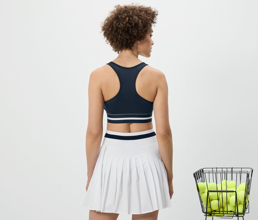 Rückansicht einer Frau, die ein blaues Sport-Bustier »Crop Top« und einen weißen Rock trägt.