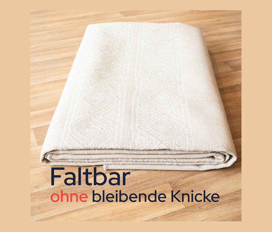 Ein grauer, faltbarer Outdoor-Teppich »Diamond Rhythm« liegt gefaltet auf einem Holzboden.