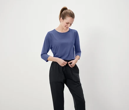 Frau justiert ihre schwarze Hose mit einem blauen Dreiviertelarm-Shirt.