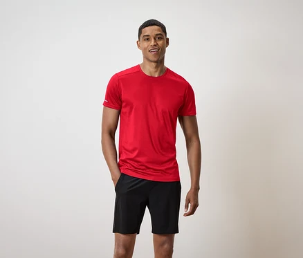Lächelnder Mann mit kurzen Haaren steht da. Er trägt ein rotes T-Shirt und schwarze Shorts.