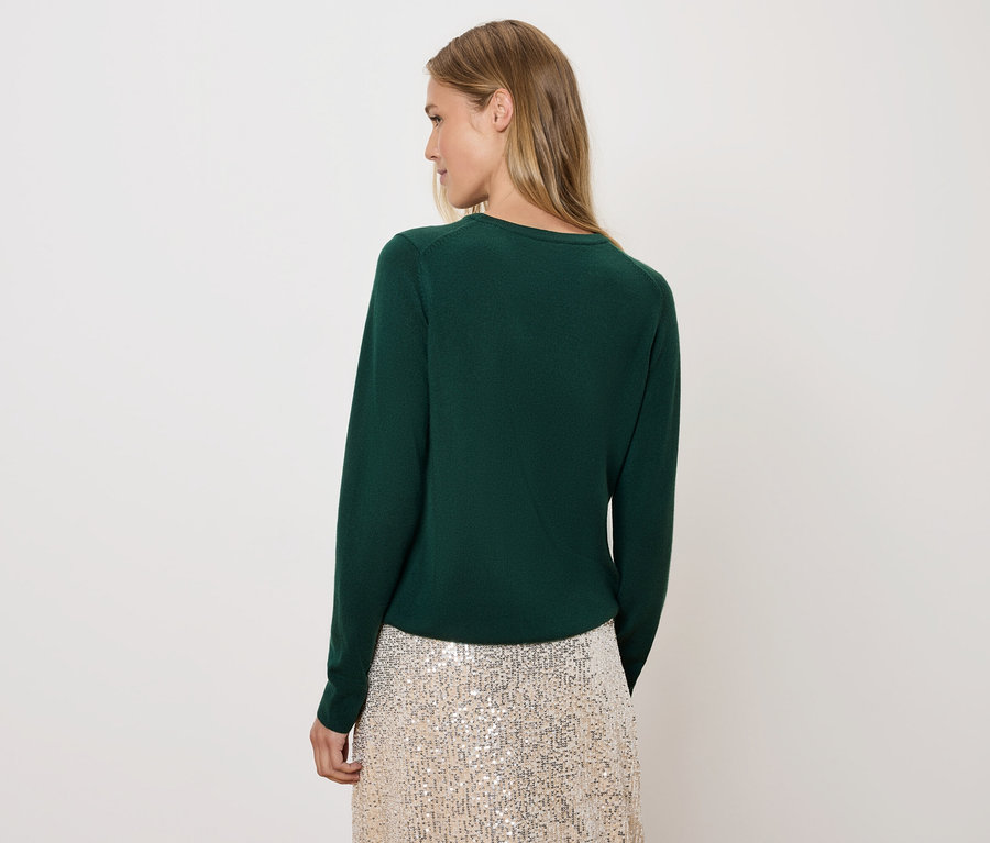 Frau blickt über die Schulter, trägt einen grünen Pullover und einen Paillettenrock.