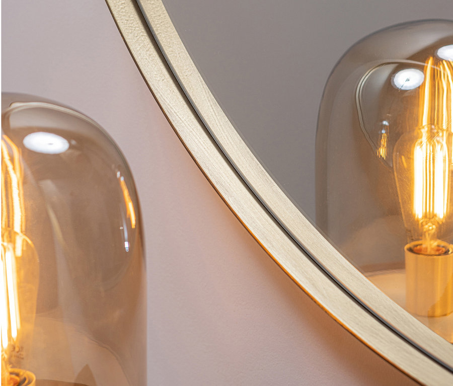 Detailansicht eines runden, goldfarbenen Woood »Doutzen« Spiegels (115 cm) neben einer Lampe.