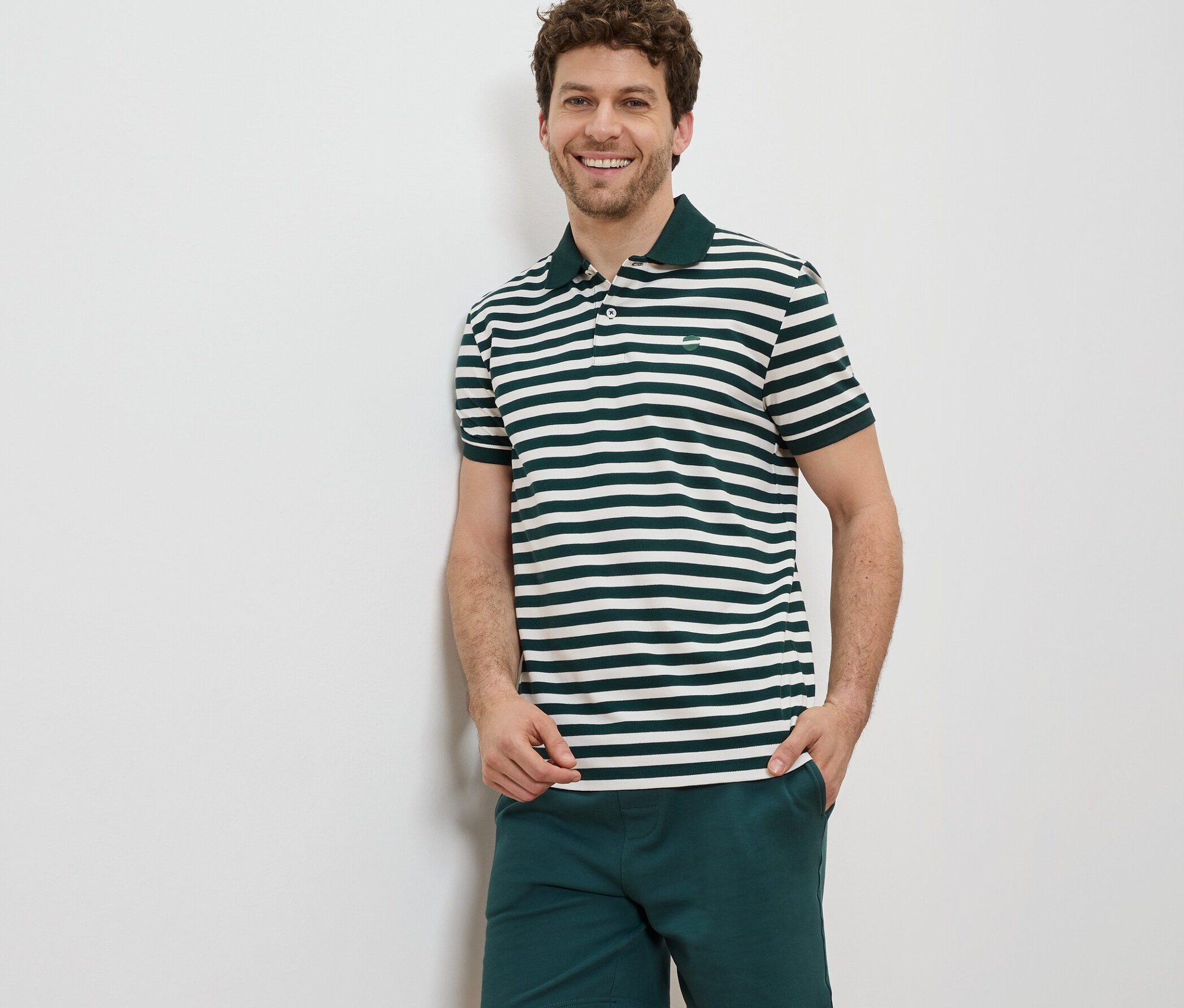 Mann steht und lächelt, er trägt ein Piqué-Poloshirt mit horizontalen Streifen und Shorts.