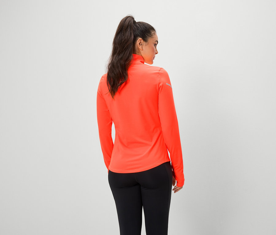 Frau mit dem Rücken zur Kamera trägt ein orangefarbenes Oberteil mit langen Ärmeln und schwarze Leggings.