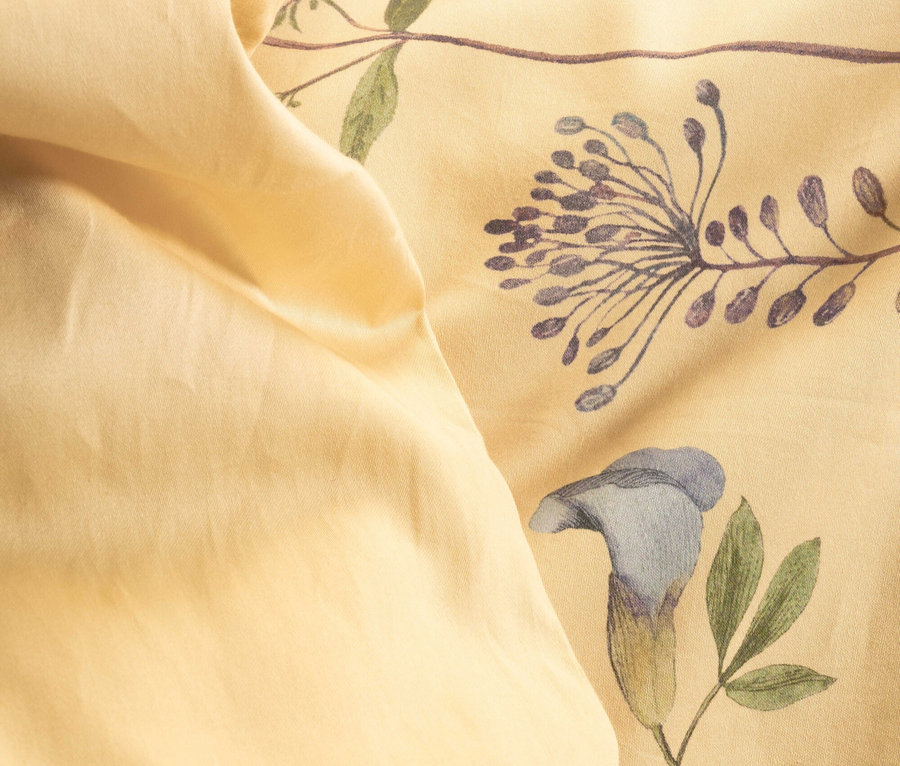 Nahaufnahme einer hellgelben Bettdecke mit Blumenmuster.