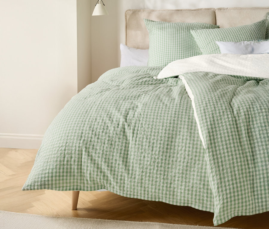 Ein Bett mit einer hellgrün-weiß karierten Bettdecke und passenden Kissen.