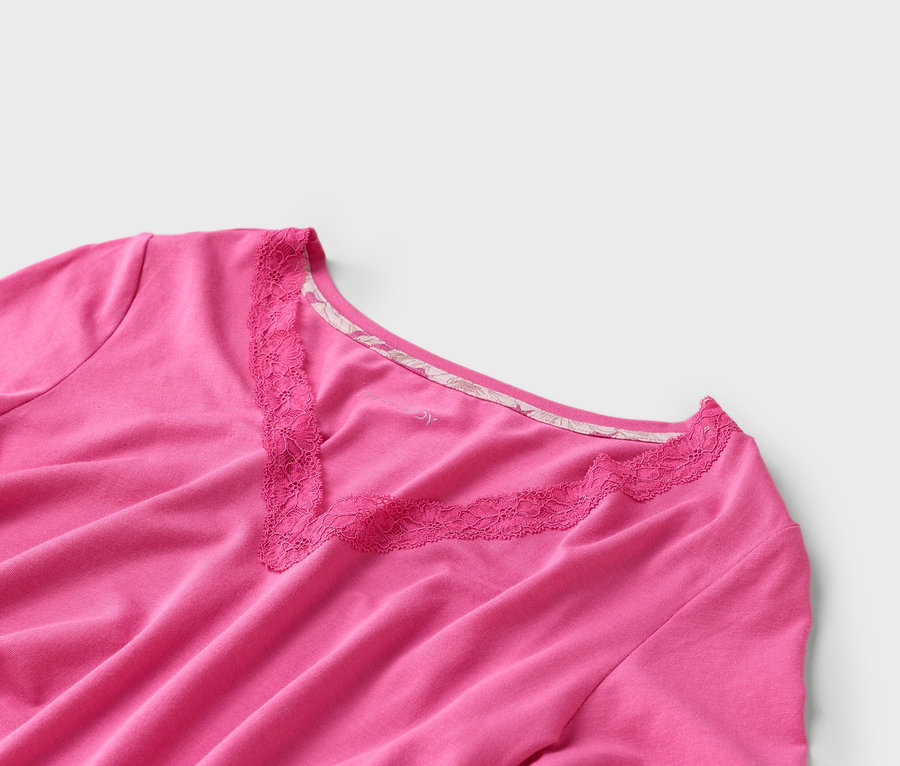 Nahaufnahme eines pinkfarbenen T-Shirts mit V-Ausschnitt und Spitzenbesatz auf weißem Hintergrund.