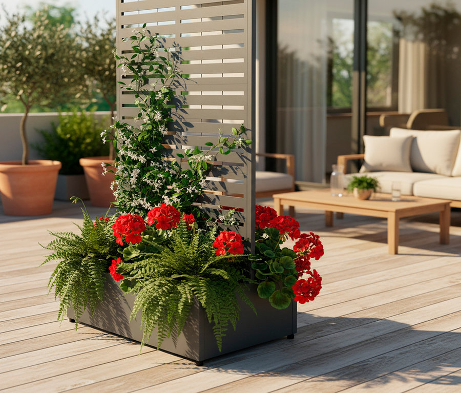 Blumenkasten mit roten Geranien und Farnen, davor ein Raumteiler aus grauem Metalllattenwerk, im Hintergrund eine Terrasse.