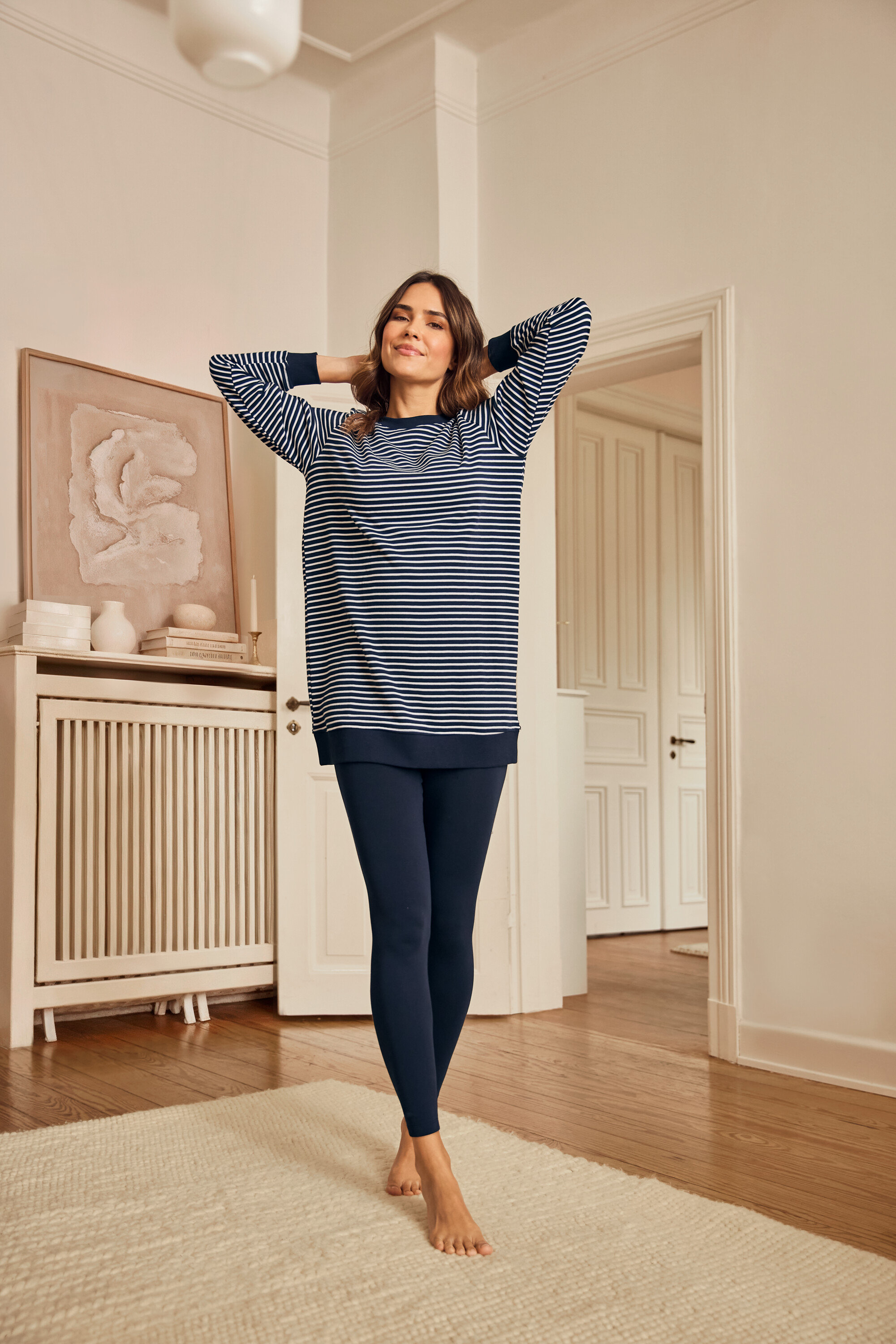 Frau mit Leggings-Pyjama steht barfuß auf einem Teppich.