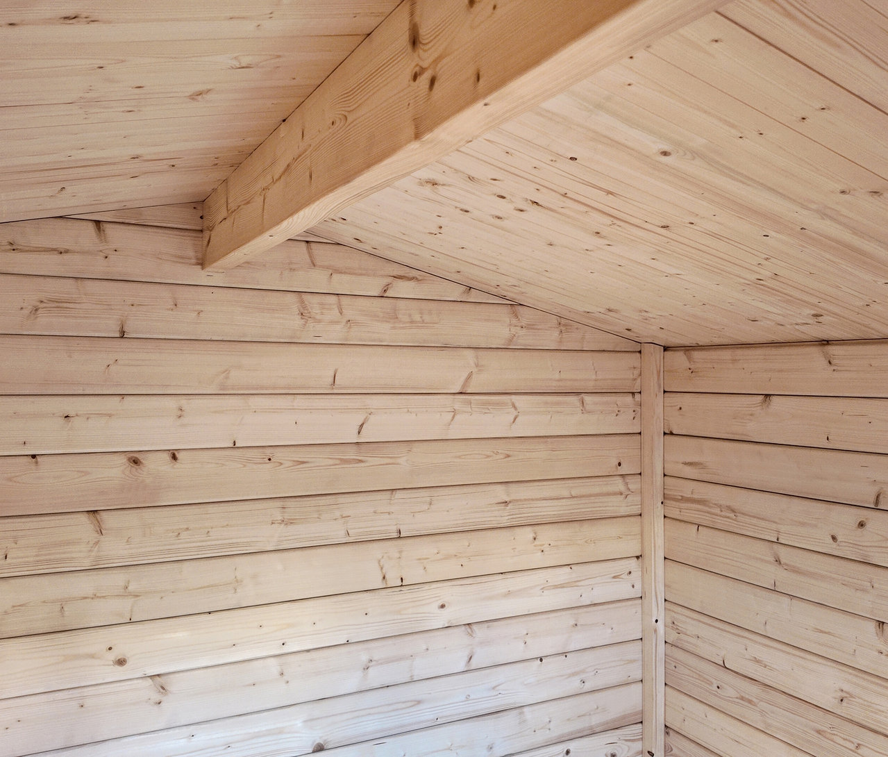 Innenansicht eines Holzhauses mit hellen Holzwänden und -decke.
