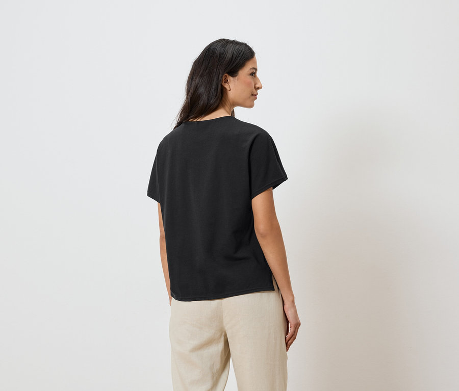 Frau trägt ein schwarzes T-Shirt und beigefarbene Hosen.