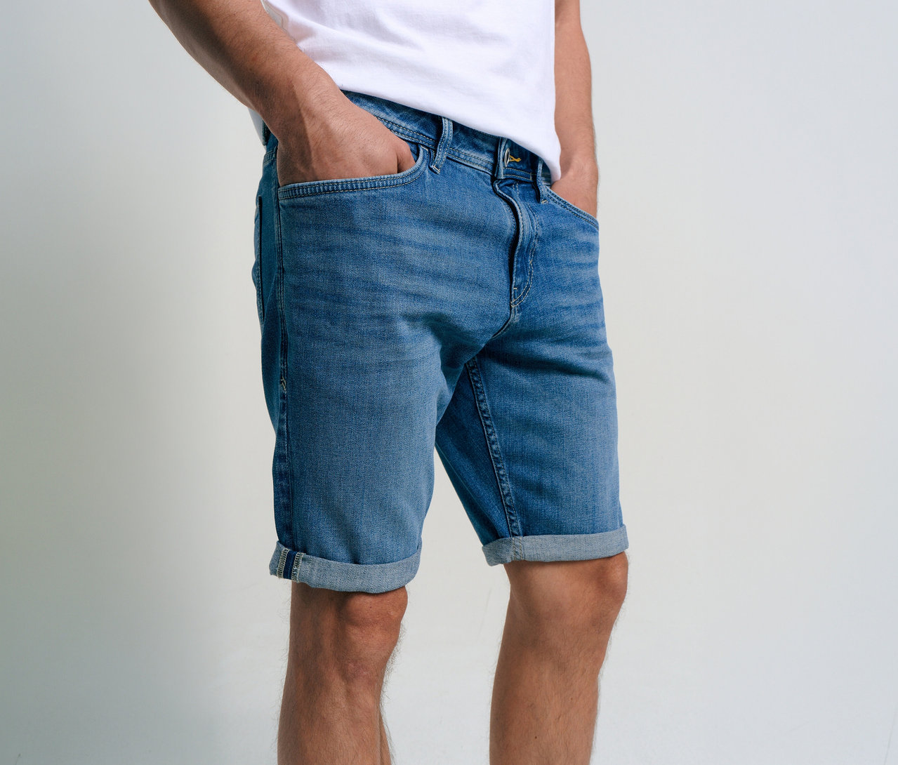 Mann mit Tom Tailor TTJOSH REGULAR SLIM Jeans Shorts in Mid Stone Bright Blue Denim mit Händen in den Hosentaschen.