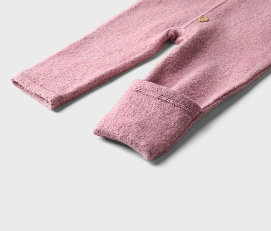 Nahaufnahme eines rosafarbenen Baby-Overalls aus strukturiertem Stoff mit umgeschlagenem Beinbund und einem Knopf.