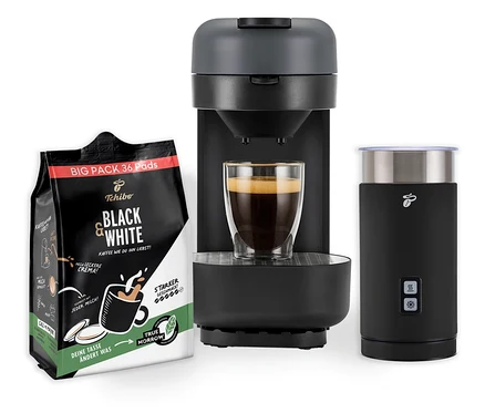 Eine Kaffeemaschine mit Milchaufschäumer und einer Tasse Kaffee steht neben einer Packung Black & White Kaffeepads.