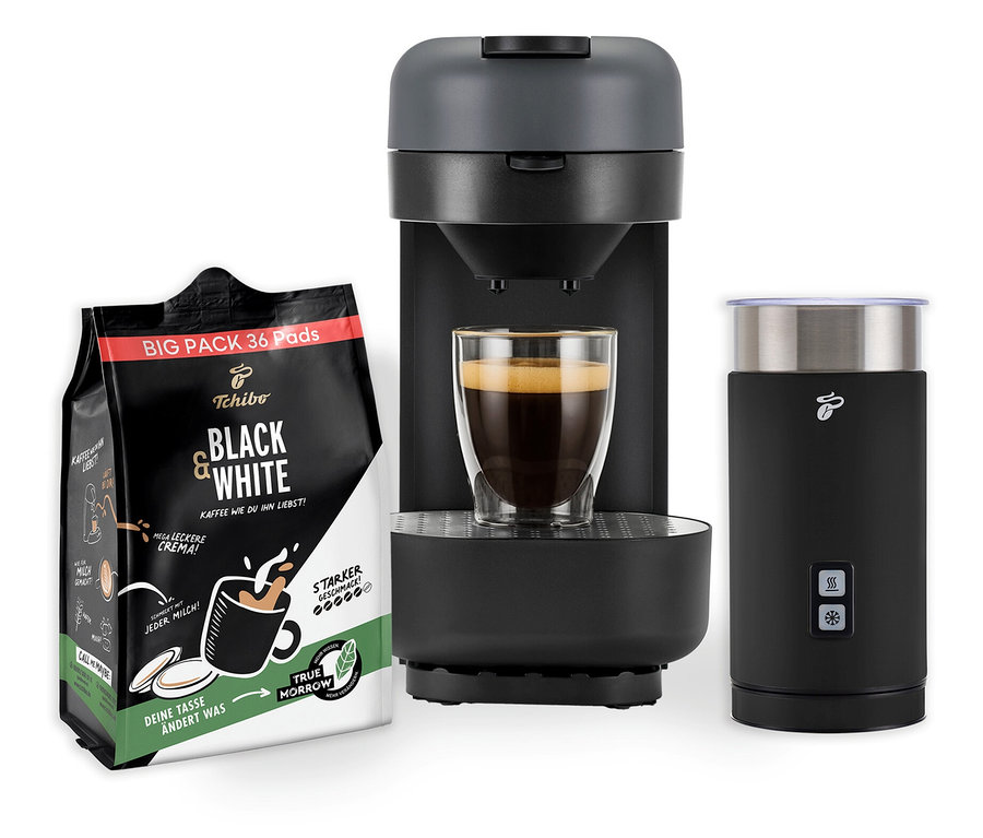 Eine Kaffeemaschine mit Milchaufschäumer und einer Tasse Kaffee steht neben einer Packung Black & White Kaffeepads.