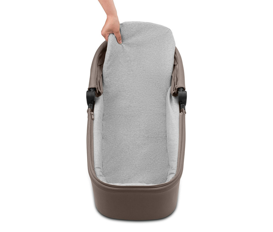 Eine Hand legt eine graue Matratze in eine braune Babywanne.