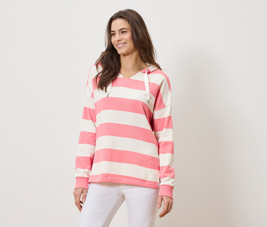 Frau trägt einen gestreiften Hoodie in Rosa und Weiß und weiße Hosen.