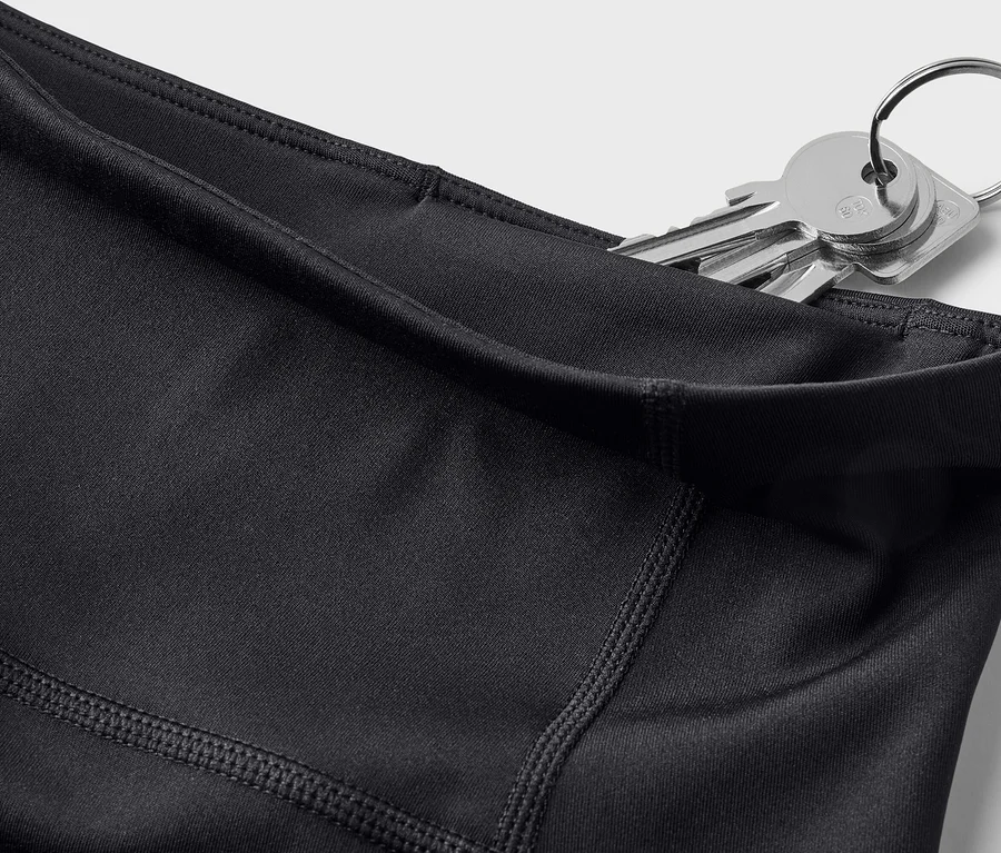 Nahaufnahme von schwarzen Leggings mit Schlüsseln in der Tasche vor einem weißen Hintergrund.