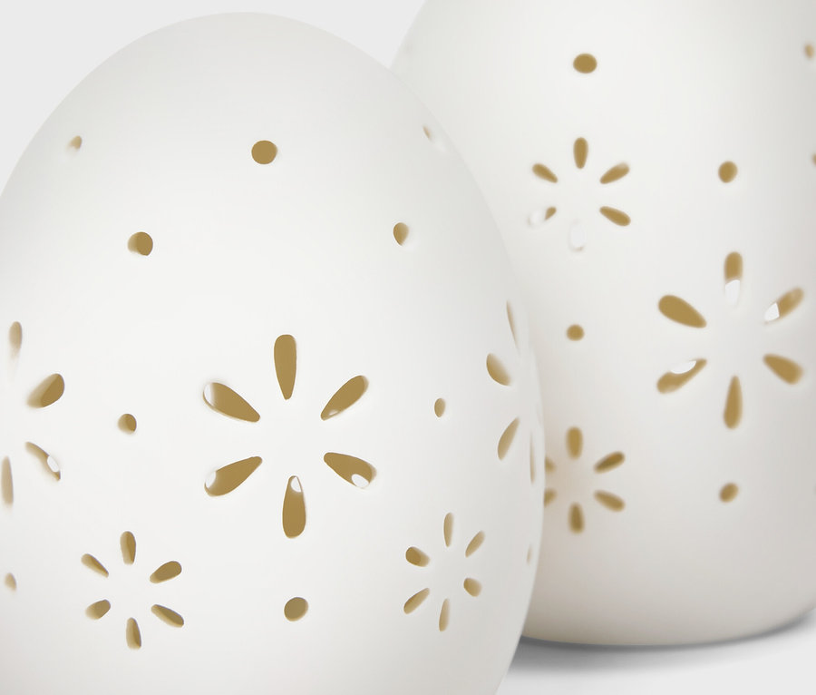 Zwei weiße, eiförmige Keramikdekorationen mit ausgeschnittenen Blumen- und Punktmustern.