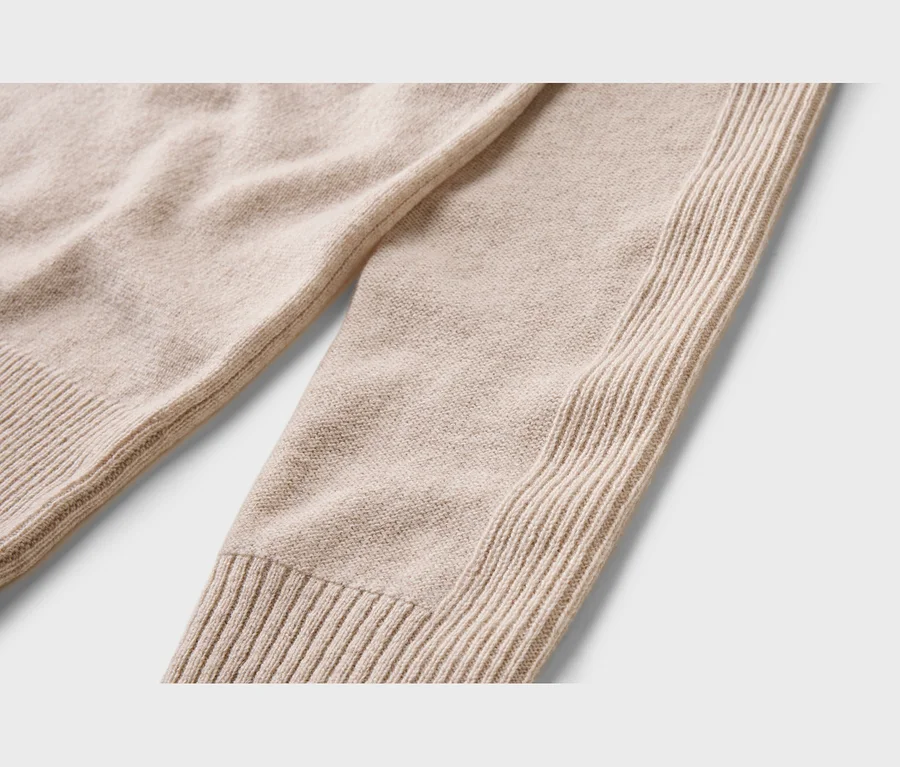Nahaufnahme eines hellbeigen Strickkleidungsstücks mit glattem Strickmuster, gerippten Bündchen und einem vertikalen Rippenmuster an der Seite.